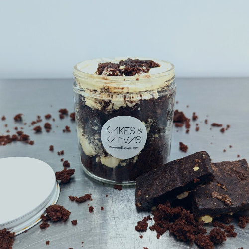 Chocolate brownie cake jar is layed cake with chocolate brownie pieces, caramel sauce, chocolate curls, and swiss meringue buttercream in a environmentally friendly reuseable glass jar