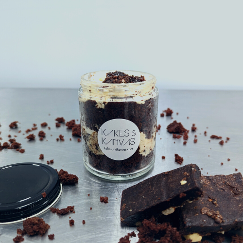 Chocolate brownie cake jar 8oz is layed cake with chocolate brownie pieces, caramel sauce, chocolate curls, andswiss meringue buttercream in a environmentally friendly reuseable glass jar